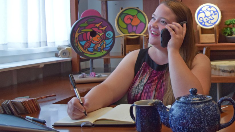 Artist Portia "Po" Chapman holding a telephone during a client art consultation at her Kingston art studio, surrounded by artwork and a teapot.