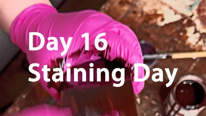 Close-up of Portia Po Chapman’s hands in pink gloves applying a dark mahogany stain to a hardwood drum frame component at Kingston Art Studio for Drum December Day 16.