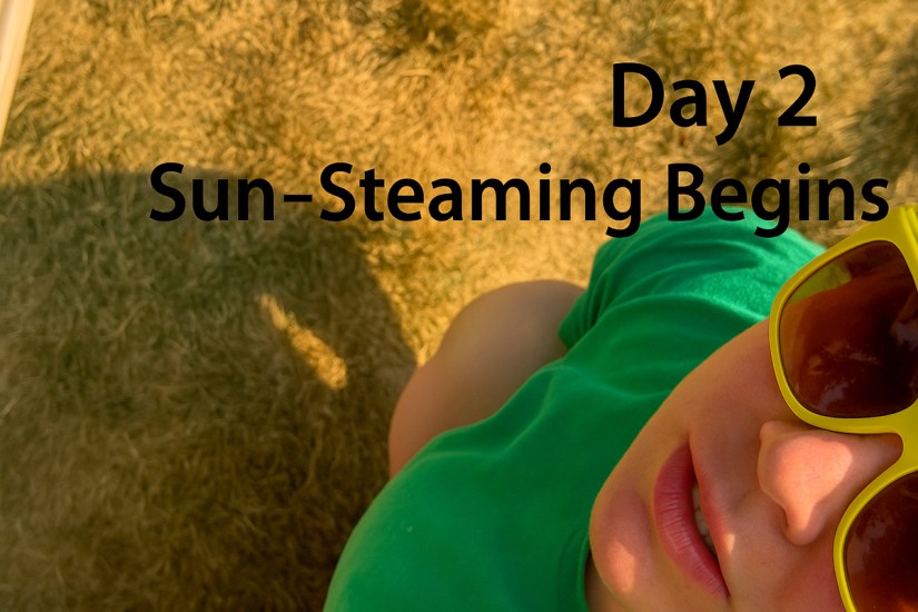 Po Chapman lying in the sun wearing yellow sunglasses and a green shirt, beginning Day 2 of her sun-steaming drum-making process.