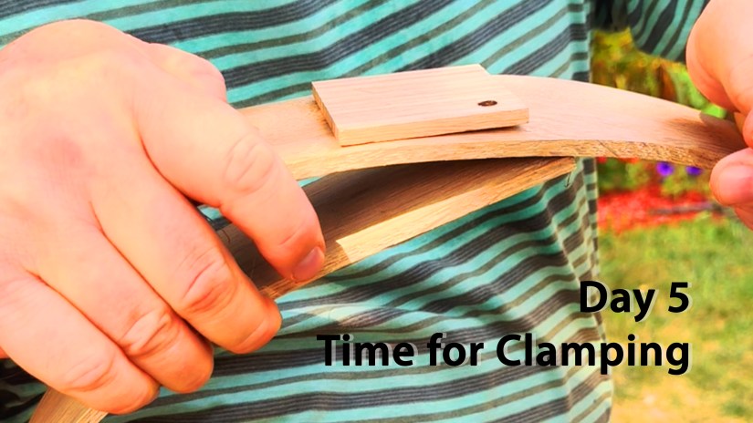 Close-up of hands holding the softened red oak board after sun-steaming, preparing the ends for clamping during Po’s frame drum-making process on Drum December Day 5.