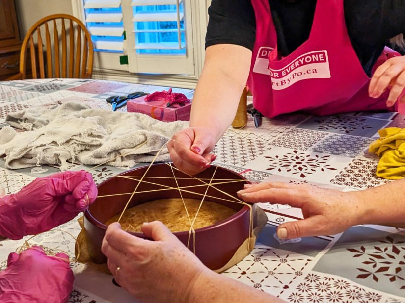 3 women stringing a 10 inch drum together while drum maker and Kingston Artist Po offers expertise and assistance.