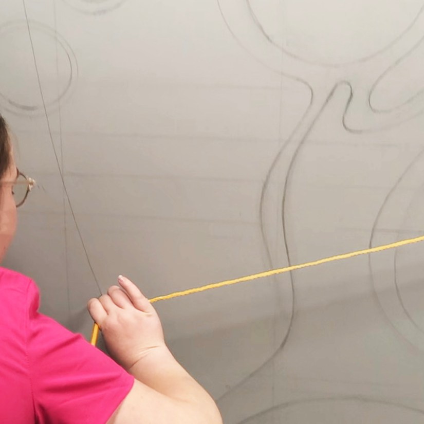 Kingston artist Portia "Po" Chapman using a custom-rigged rope and pencil compass to draw precise concentric arcs for the Strong Enterprises mural.