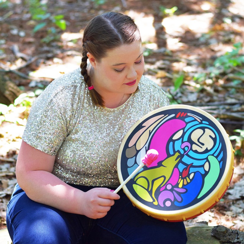 Kingston Artist Portia “Po” Chapman holding and drumming the "Elder in Residence" painted rawhide frame drum, part of the permanent art collection at Queen’s University Faculty of Education.