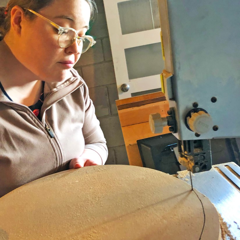 Kingston artist Portia "Po" Chapman using a shop band saw to precisely cut circular discs from 3/4 inch exterior MDO signboard for the Sensory Garden installation.