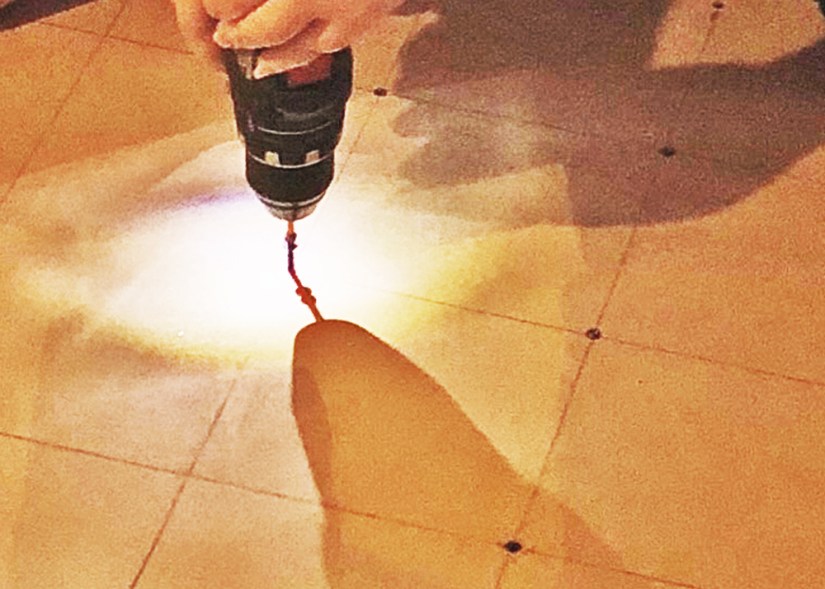 A close-up process shot showing Portia Chapman driving screws into a 2-ply MDO sign board in a 5" x 5" grid pattern to create a solid 1.5" thick mural substrate.