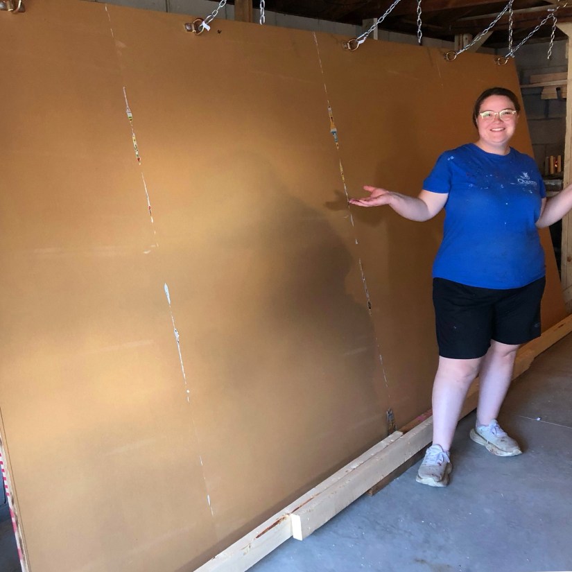 Artist Portia Chapman standing with a large, 2-ply staggered-seam sign board mounted on a custom-built structural beam easel in her studio.