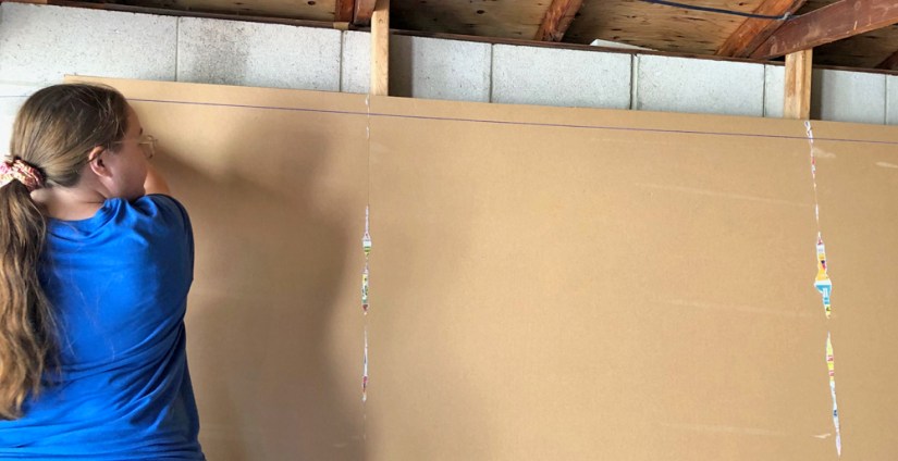 Kingston Artist Portia Chapman snapping a blue chalk line across a 14-foot primed board to establish a perfectly level horizontal axis for the "Strong and Growing Stronger" mural.