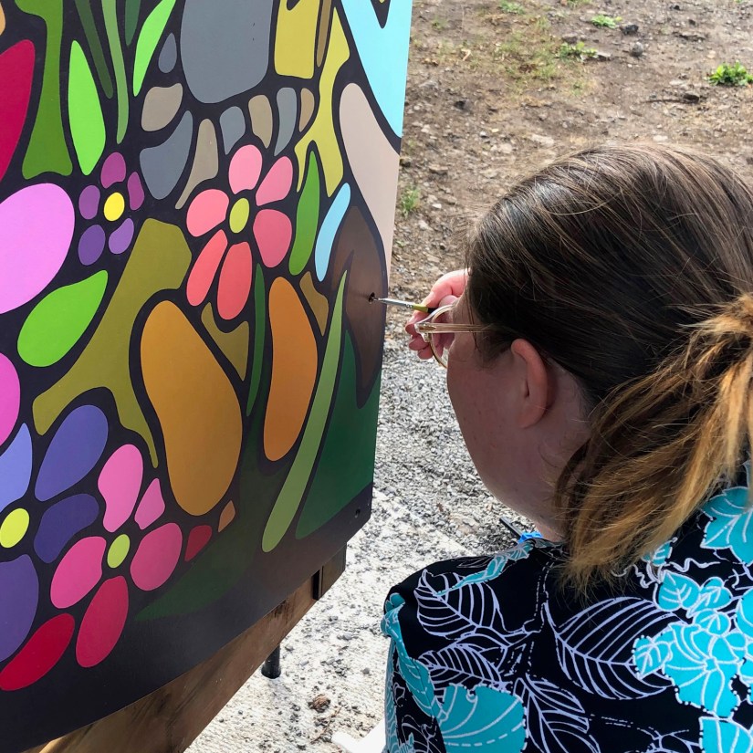 Kingston Artist Portia “Po” Chapman performing precision touch-ups on the installed "Exploring the Senses" mural at Base31 Sensory Garden, using a small round artist brush to ensure a perfect execution of the storytelling art.