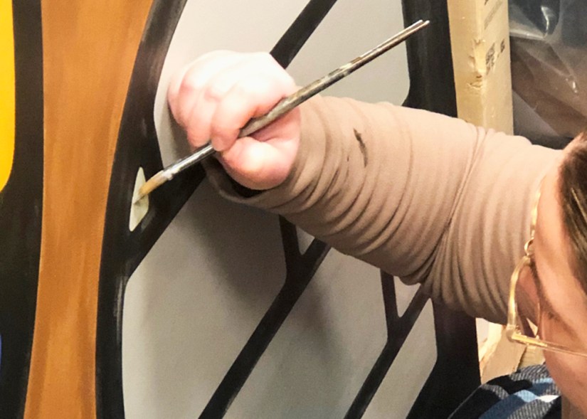 Kingston Artist Portia Chapman using a small round brush to paint a 14' x 6' mural, demonstrating her specialized technique for achieving flat, ridge-free transitions between colours.