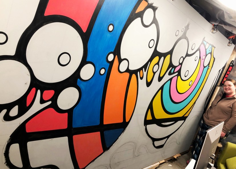 A process photograph showing semi-transparent layers of paint being applied to a mural, demonstrating Kingston Artist Portia Chapman’s technique for achieving high opacity with minimal brush texture.