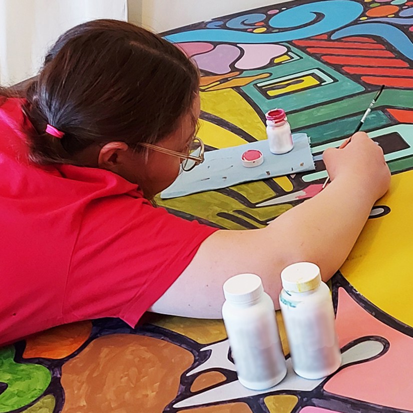 Kingston Artist Portia “Po” Chapman freehand painting the 3D "Building a Bright Future" mural for Base31, using small round brushes to apply hand-mixed acrylics to a 6-foot diameter frame-drum-inspired structure.