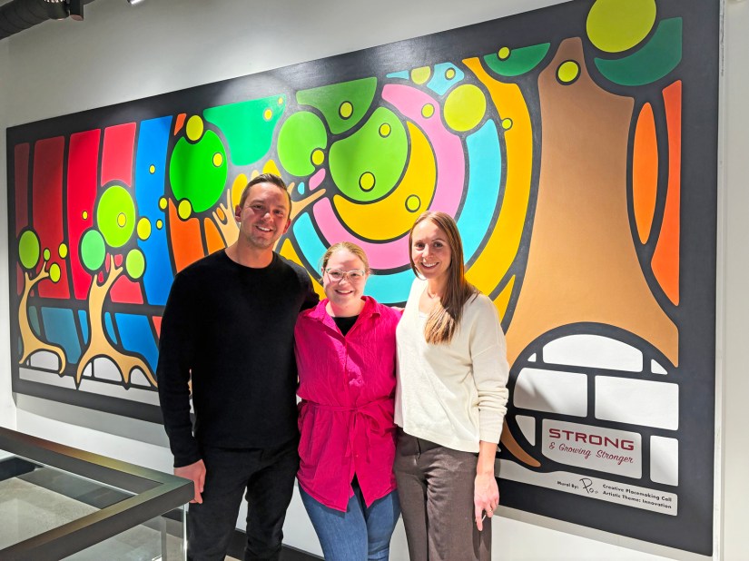 Professional artist Portia "Po" Chapman standing between Strong Enterprises CEO Justin Strong and COO Natalie Strong in front of the completed Storytelling Art mural.