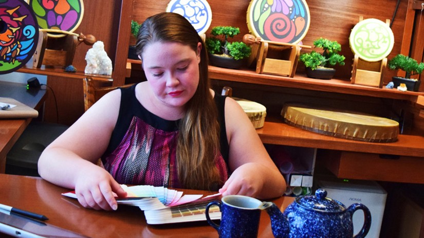 Portia "Po" Chapman, Kingston Artist, at her Kingston Art Studio desk reviewing colour palettes, surrounded by painted rawhide drums and nature-focused illustrations for her Research & Project Archive.