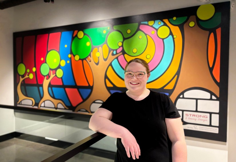 Portia “Po” Chapman, Kingston Artist, stands in front of her 14'X6' Storytelling Art mural "Strong and Growing Stronger" at Strong Enterprises HQ, demonstrating professional creative placemaking and large-scale project execution.