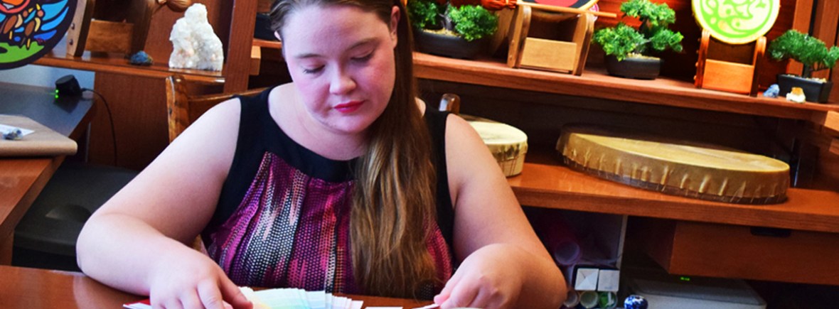Portia "Po" Chapman, Kingston Artist, at her studio desk reviewing color palettes, surrounded by painted rawhide drums and nature-focused illustrations for her Research & Project Archive.