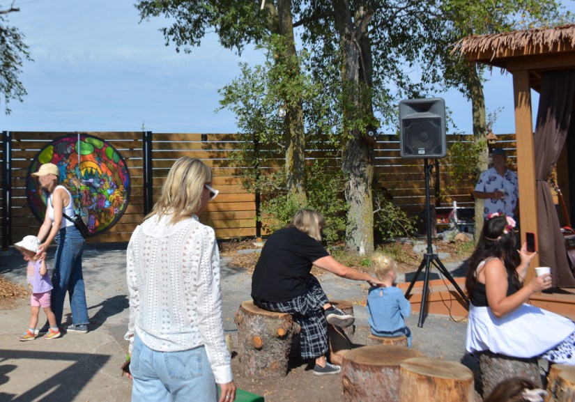 Attendees of all ages listening to Kingston artist Portia "Po" Chapman public speaking about the the mural, "Exploring the Senses," featured on a fence in the background.