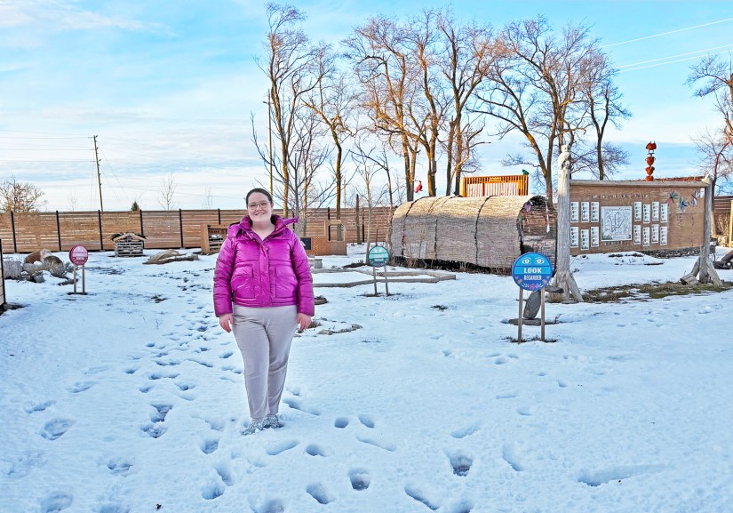 Kingston artist Portia "Po" Chapman standing in the snow-covered Sensory Garden at Base31 in January 2026, surrounded by vibrant, weather-resistant station signs.