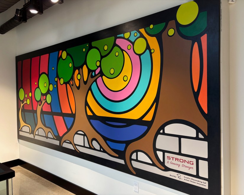 A right-side perspective of the 14' x 6' mural titled "Strong and Growing Stronger" by Portia Chapman, showing the seamless hand-painted texture and integrated typography at Strong Enterprises HQ.