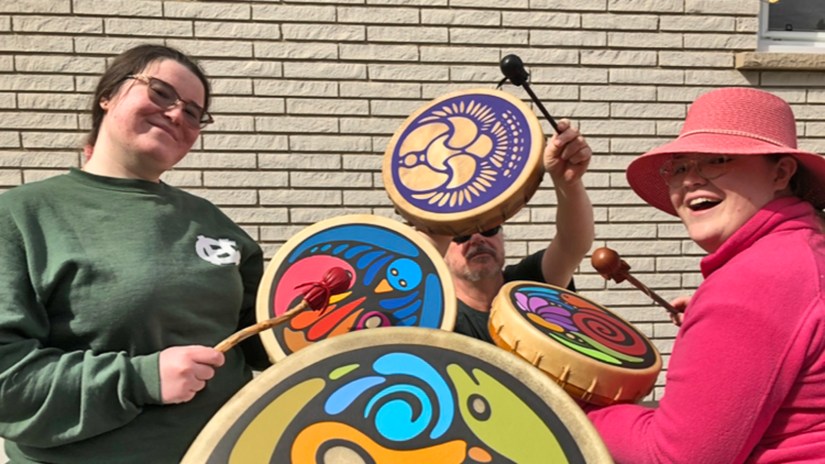 Kingston artist and drum making expert Portia “Po” Chapman drumming outdoors with her family at her art and drum-making studio. In the background, her father drums on his purple "Ruffed Grouse" frame drum, representing his recovery from a closed head injury and PTSD through rhythmic healing.