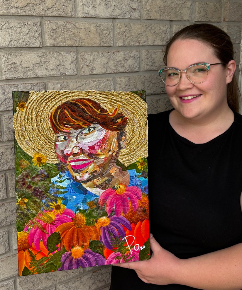 Artist Portia "Po" Chapman holding her mixed media portrait "Meeting Mary," featuring a sunhat made of rope, vibrant floral collage, and dried flowers set against a stone brick wall.