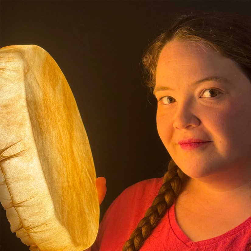 Kingston artist Portia Po Chapman standing beside an illuminated rawhide frame drum in her glowing art installation Being Seen at the Tett Centre Pocket Gallery.
