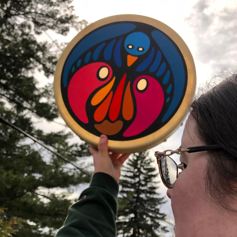 Kingston artist and frame drum maker Portia Po Chapman holds up a vibrant hand-painted drum as natural sunlight illuminates the unpainted rawhide eyes and face.