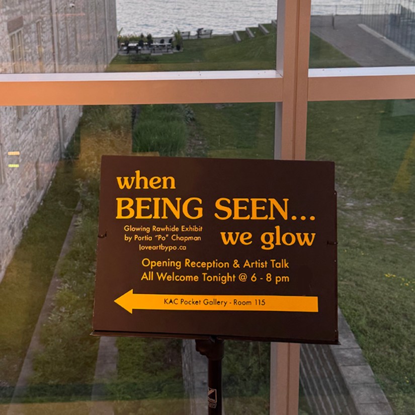 Custom black and gold directional sign in the Tett Centre foyer for Being Seen opening reception by Kingston artist Portia Po Chapman pointing toward the KAC Pocket Gallery.