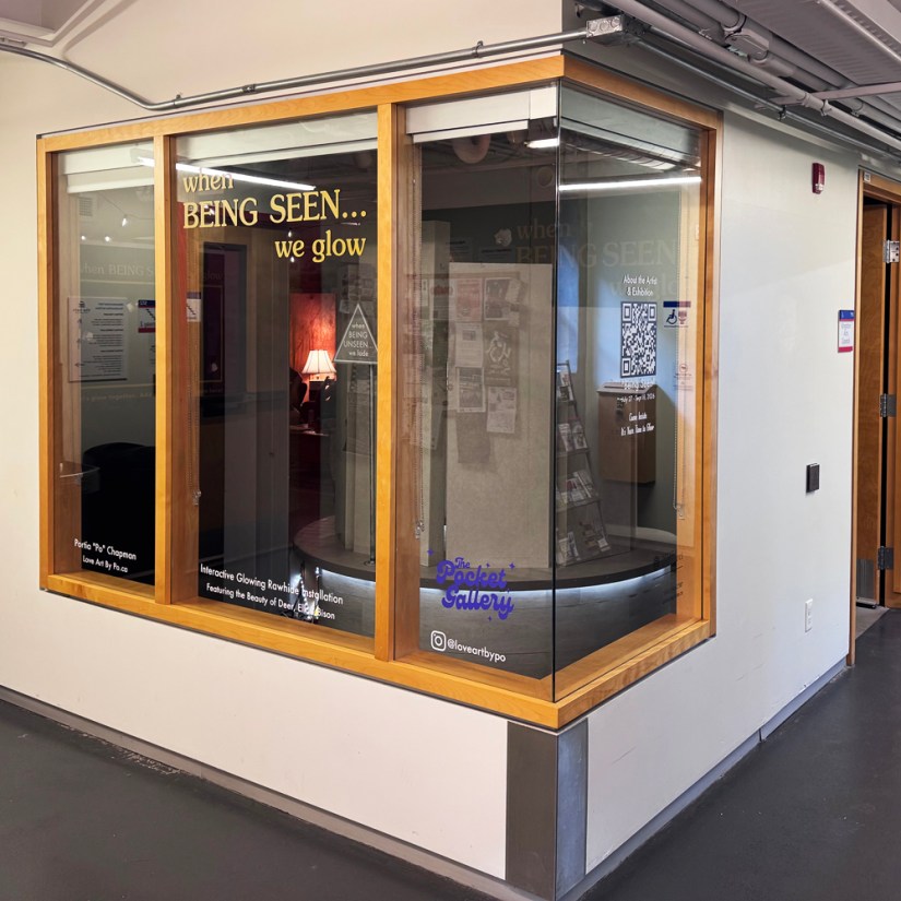 Exterior wide-angle view of the Pocket Gallery corner glass windows at the Tett Centre displaying exhibition vinyl typography and a scannable QR code poster for exhibition details by Kingston artist Portia Po Chapman.