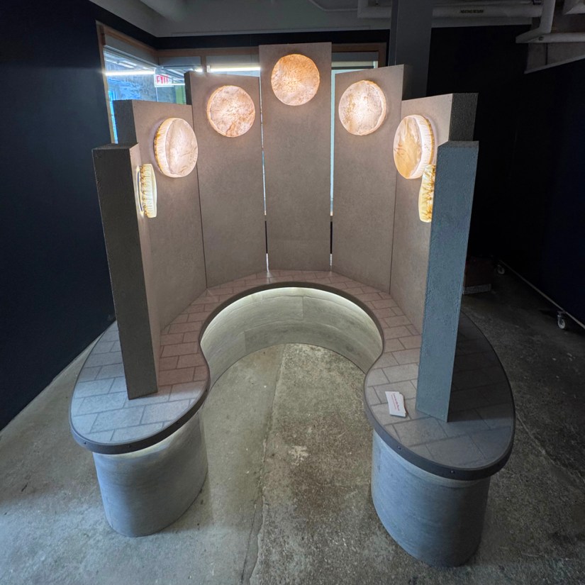 The completed Glow Chamber sculpture glowing softly in the Pocket Gallery with all seven rawhide vessels illuminated against textured monoliths and business cards placed on the tiled plinth.