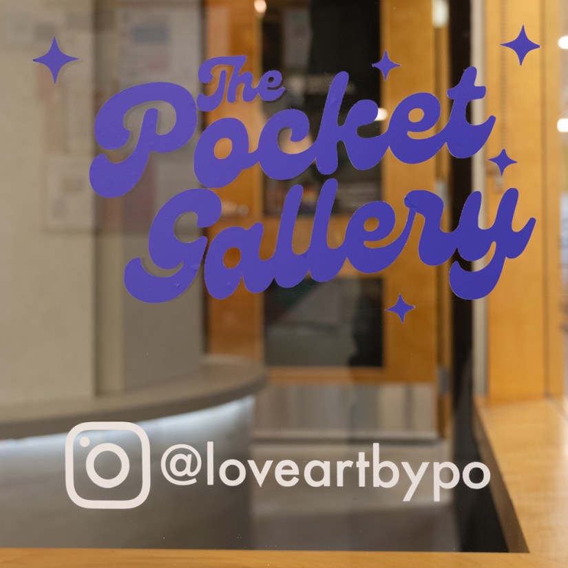 Close-up view of the bottom right gallery window at the Tett Centre displaying artist Portia Po Chapman's white Instagram decal @loveartbypo positioned directly beneath the permanent purple Pocket Gallery logo.