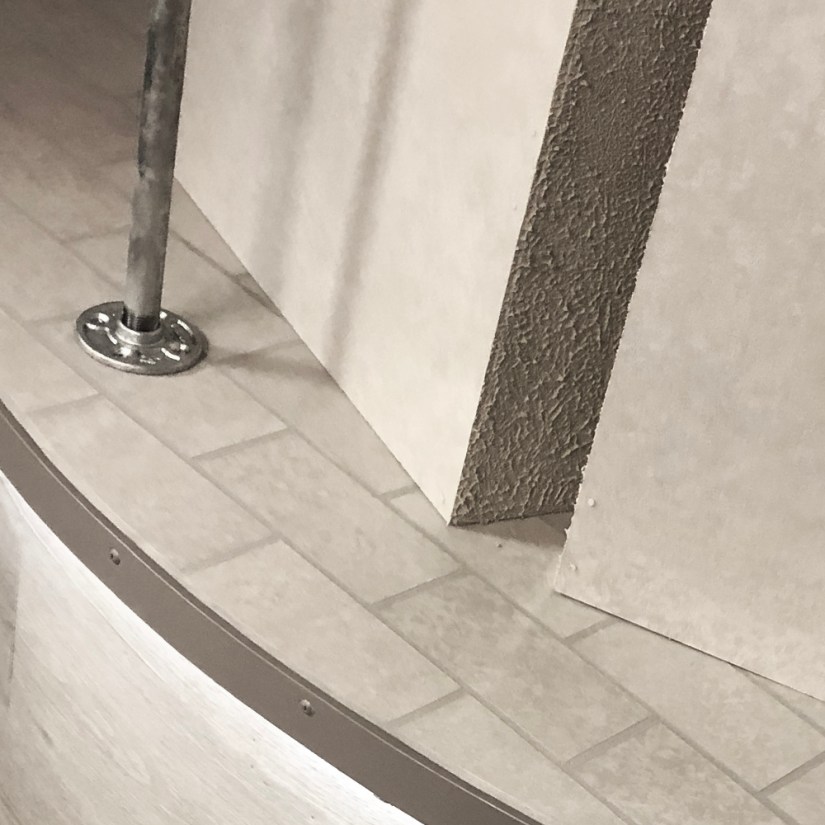 Rear perspective of the Glow Chamber installation featuring grey oak-look wrapped plinth walls, troweled stone texture on monolith sides, and cool grey under-lighting.