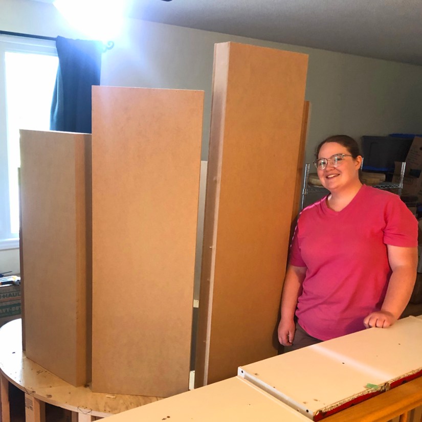 Artist Portia Po Chapman standing proudly next to three tall, hollow MDF monolith structures mounted on a wooden base in her studio.